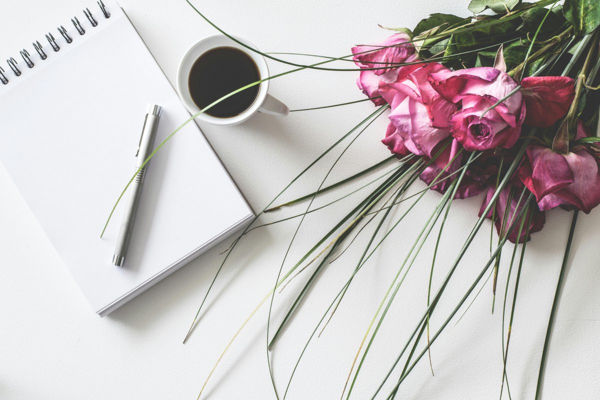 A note pad and pen, a coffee cup, and a bouquet of pink roses