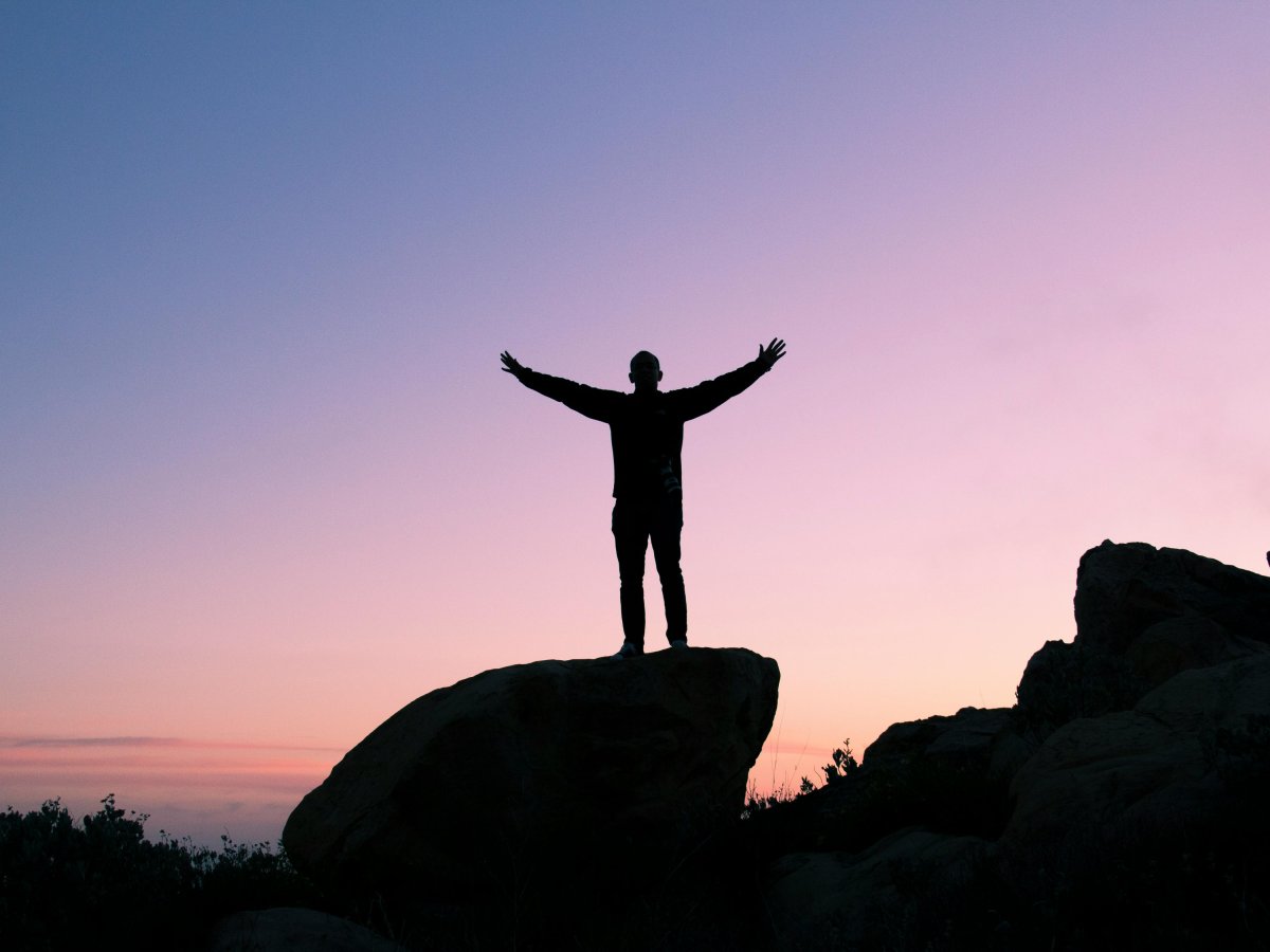 A black silhouette of a man with arms outstretched with a sunset in the background.